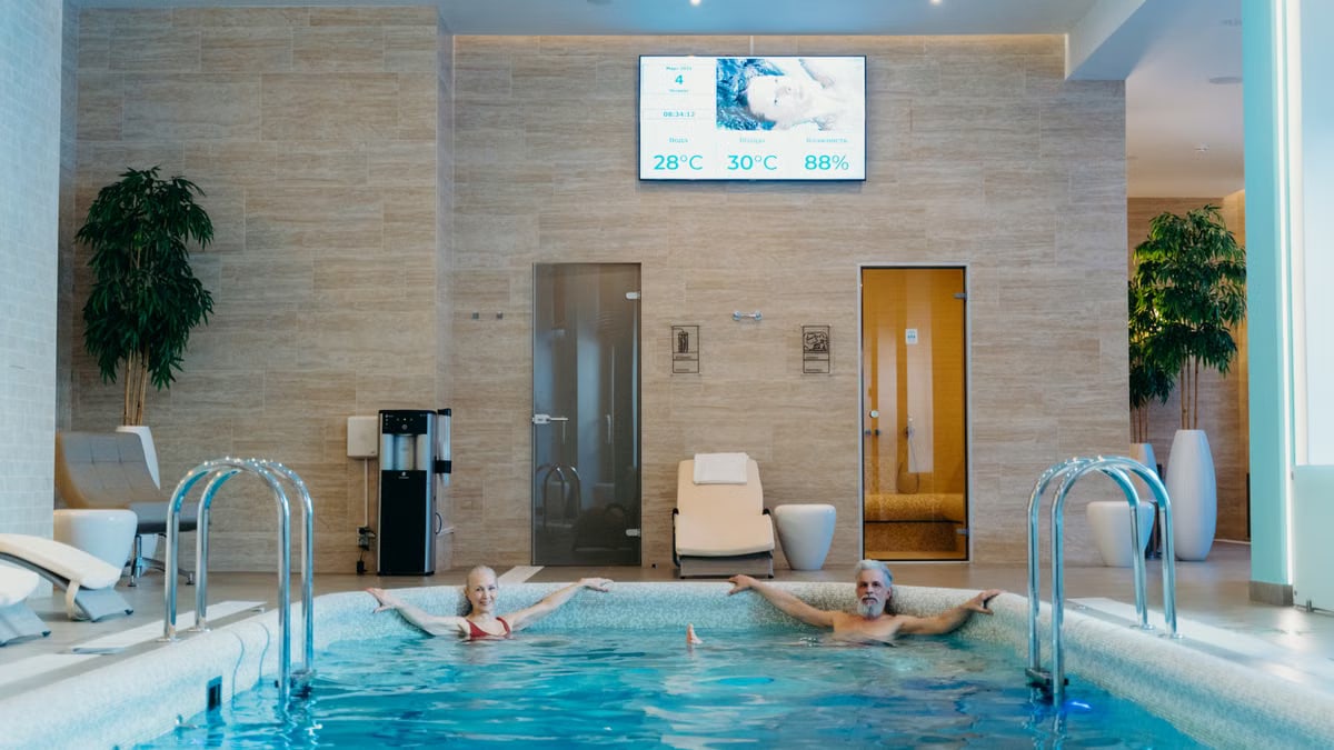 Two adults enjoying leisure time at an indoor swimming pool with spa-like ambiance.